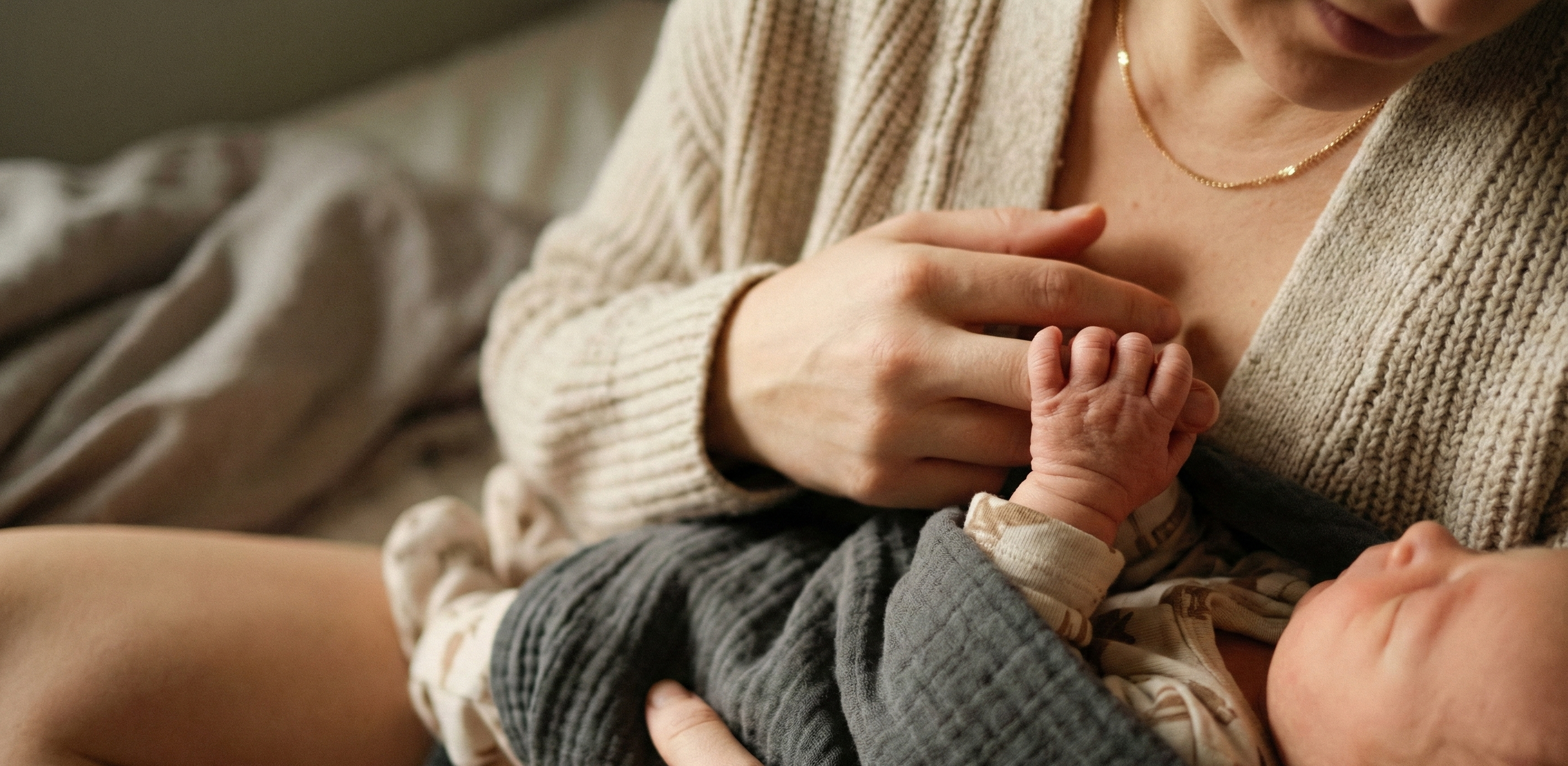Mother tenderly holding newborn with baby gripping her finger
